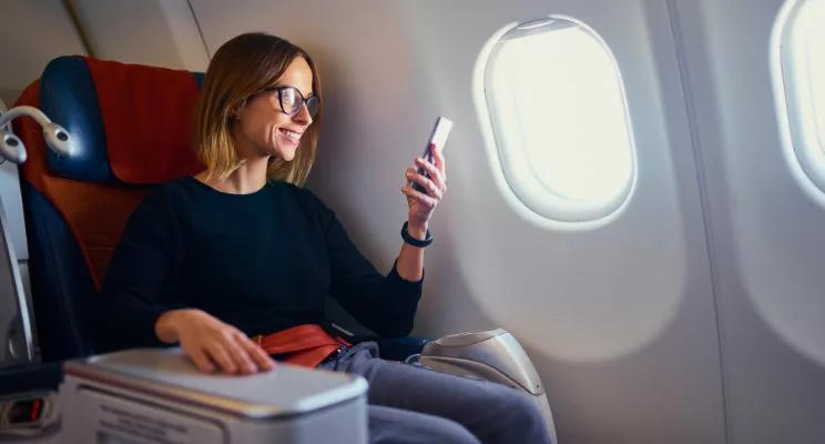 Woman with glasses smiling at her phone sitting in an airplane seat